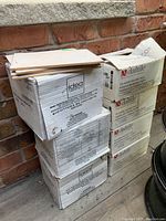 Stack of seven boxes of ceramic tiles including Daltile and Idea Ceramica brands, some tiles placed on top for display.