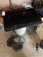 Dynex 26-inch TV angled view on a trash bin with four car speakers and power cord visible below