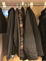 Five winter jackets hanging from a rack, various dark colors including a camouflage jacket and one with fur-lined hood.