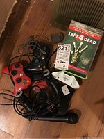 Multiple Xbox controllers, Left 4 Dead game and motion controller accessories arranged on wooden floor.