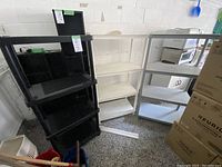 View of three shelving units side by side: black, white, and gray plastic shelves in garage space.