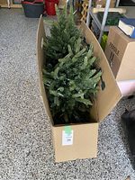 Artificial Christmas tree packed inside open cardboard box showing the branches and pine needle tips.