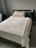 Full view of the black queen bed frame assembled with mattress, bedding, and pillows on top. The bed is made and shows beige and white bedding with pillows.