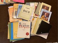 Top view showing the collection of sheet music books and booklets spread out on the floor, highlighting covers of Bach, François Couperin, and The Beatles.