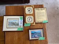 Four decorative items displayed on a wooden surface: barometer and thermometer mounted on wood with brass corners, plaque with poem, two framed prints of harbor and town scenes.