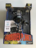 Front view of boxed Robby The Robot toy with visible robot inside plastic window. Box has 'Forbidden Planet' branding and features describing light, sound, and walking functionality.