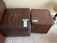 Two brown ottomans side by side on carpet. Larger leather ottoman shows wear, smaller fabric ottoman has storage inside.