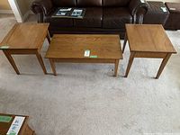 Set of 3 wooden tables on carpeted floor: two square end tables and one rectangular coffee table.