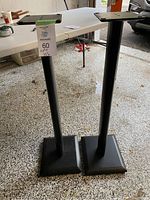 Two black Sanus speaker stands side by side, showing overall height and base shape.