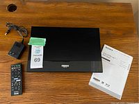 Sony Ultra HD Blu-ray/DVD player on wood surface with power adapter, remote control, user manual and auction lot tag.