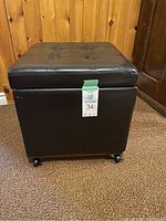 Full view of black square faux leather ottoman on caster wheels