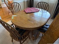 Oval wood dining table with six matching chairs and black seat pads, set in a room with hardwood floor and carpet.