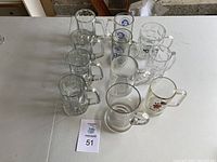 Overview of 11 assorted beer glasses on table, includes clear glass mugs and Mickey Mouse design mug.