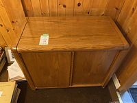 Wood cabinet with a smooth top and two front doors, showing wood grain and rounded edges.