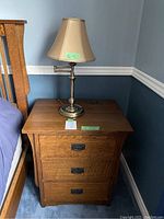 Front view of oak nightstand with three drawers and lamp on top