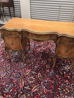 Full view of the French Provincial style desk showing the ornate curved wood top, carved details, and drawer fronts against a patterned rug.
