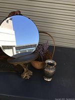 Round wall mirror with gold-tone ornate shelf, tripod base, held against a light-colored background.