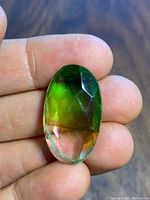 Image showing the oval faceted tourmaline held between fingers, displaying its green to orange color gradient and transparency.
