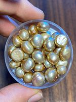 Clear top-down image of container with various irregular champagne-colored pearls showing their luster and shapes.