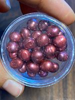 Close-up photo of a container filled with loose purple freshwater pearls, showing their size, shape, and color.