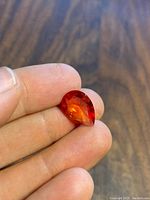 Close-up of pear-shaped orange-pink lab Padparadscha sapphire held between fingertips showing facets and clarity.
