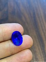 Close-up photo showing deep blue oval faceted lab sapphire held between fingers, highlighting color and cut.