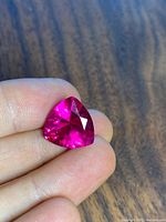 Close-up front view of the 4.0 Ct pink lab-created ruby gemstone held between fingers, showcasing vibrant pink color and triangular cut.