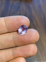 A clear close-up image of an oval cut ametrine gemstone resting on a finger, showing facets and light purple color.