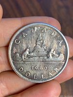 Obverse side showing 1960 Canadian silver dollar coin with canoe and maple leaf design.