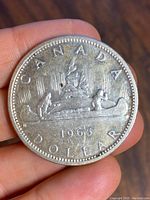Obverse of 1965 Canadian silver dollar showing a voyageur canoe design, held in hand.