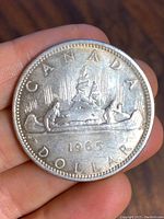 Reverse side of the 1965 Canadian silver dollar displaying a canoe with voyageurs, maple leaves, and the year 1965.