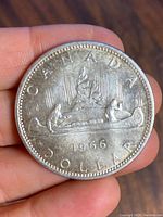 Reverse side of the 1966 Canadian silver dollar coin showing a canoe with paddlers and inscriptions.