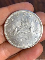 Front side of 1966 Canadian silver dollar coin showing two paddlers in a canoe with rays in the background and the text 'CANADA DOLLAR 1966'.