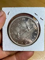 Reverse side of the 1965 Canadian silver dollar coin displaying a canoe with two men paddling and inscriptions.