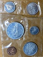 Top view of sealed 1965 Canadian uncirculated coin set showing several coins including 1 cent, 5 cents, quarter, and large dollar coin in plastic encapsulation.