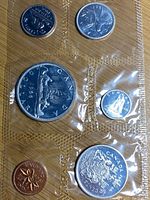 Photo showing front side of Canadian coins in original vacuum-sealed packaging, displaying detailed coin faces including maple leaf and canoe designs.