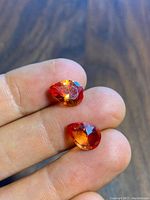 Two faceted lab Padparadscha sapphires in hand showing overall color and shape.