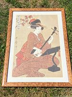 Overall view of the framed vintage Japanese print showing a woman playing the shamisen outdoors on grass.