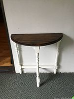 Front view of the antique half moon hallway table showing the dark wood top and white painted legs.