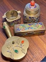 Overview of four brass and cloisonné enamel smoking set items including ashtray, lidded container, pipe handle, and rectangular box.