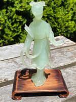 Front and angled view of the pale green translucent carved jade figure of a lady in traditional dress on a wooden base, highlighting detailed robes and hair ornament.
