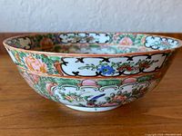 Side view of the large Chinese rose-medallion bowl showing intricate floral and bird designs with a vivid color scheme of pinks, greens, blues, and gold accents.