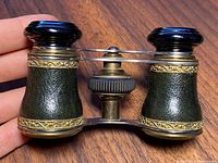 Pair of tapered opera glasses with leather covering, gold gilt decorative bands, black eyepieces, and brass and black focusing mechanism.