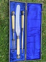 Photo of antique silver and stag handled carving set in original box, showing knife, fork, and sharpening steel with detailed silver and stag handles inside a blue fabric lined box.
