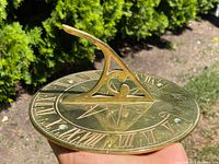 Top angled view of the solid brass sundial showing raised triangular gnomon and Roman numeral markings around dial edge.