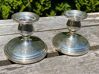Pair of antique sterling silver candlesticks on a wooden surface, showing polished finish with minor tarnishing and patina
