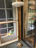 Full view of the antique torchiere floor lamp near a door, showing height and setting.