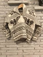 Front view of authentic Cowichan sweater showing wool knit with thunderbird and geometric patterns, ribbed cuffs and waistband, shawl collar with button, cream and brown colors.