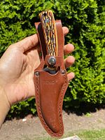 Folding knife inserted and secured in brown leather sheath with stitching and snap button closure, embossed 'ROKCO'
