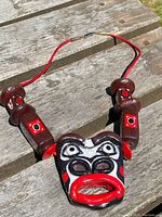 Front view of handmade Northwest Coast necklace featuring painted carved face pendant on red cord.